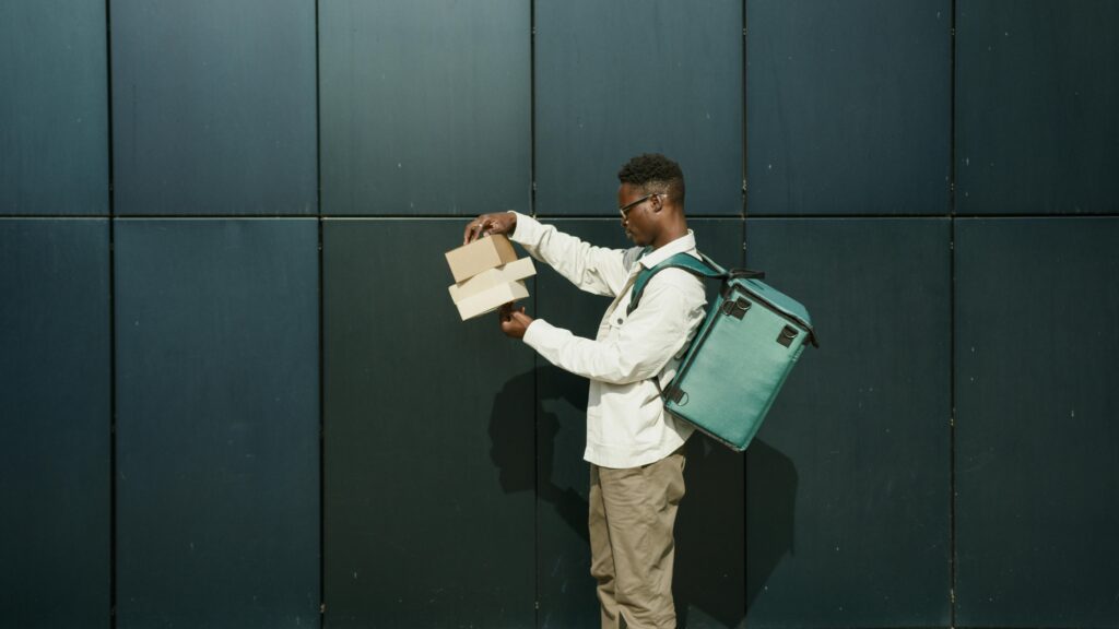 African American delivery man holding packages against an urban backdrop outdoors.